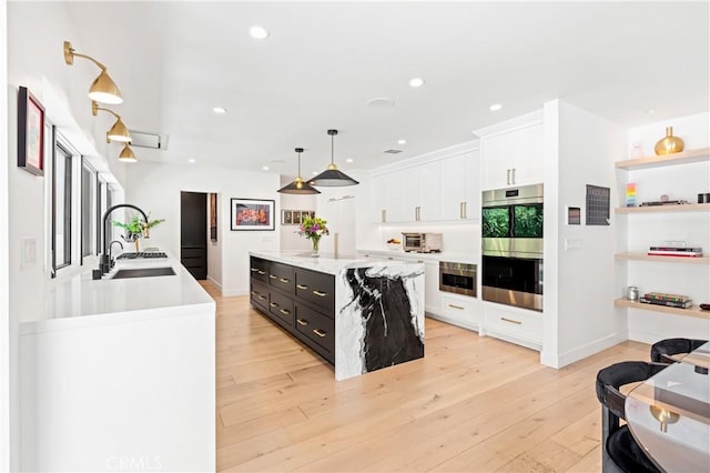 kitchen featuring decorative light fixtures, sink, white cabinets, a kitchen island with sink, and stainless steel double oven