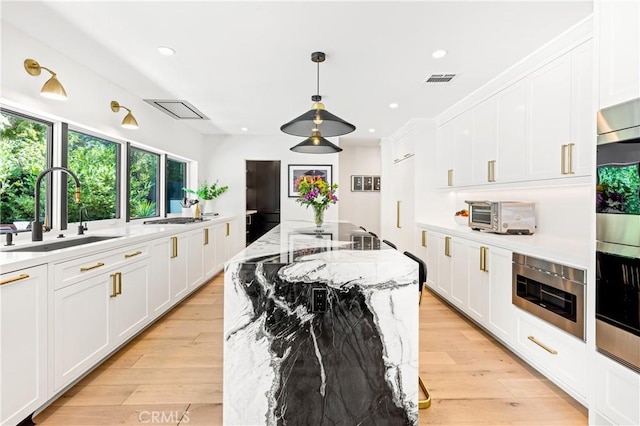 kitchen featuring white cabinetry, sink, a kitchen island with sink, light stone counters, and light wood-type flooring