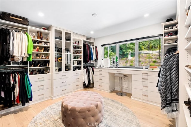 spacious closet with built in desk and light hardwood / wood-style flooring