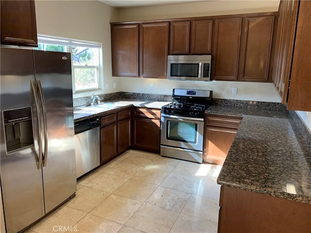 kitchen featuring sink, light tile patterned floors, stainless steel appliances, and dark stone counters