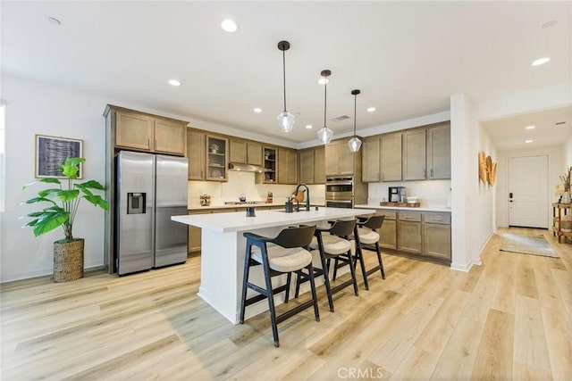 kitchen featuring light hardwood / wood-style flooring, a breakfast bar area, appliances with stainless steel finishes, a kitchen island with sink, and decorative light fixtures