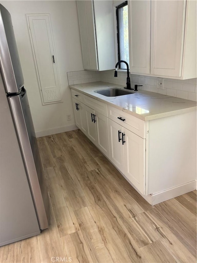 kitchen featuring sink, stainless steel fridge, white cabinetry, backsplash, and light wood-type flooring