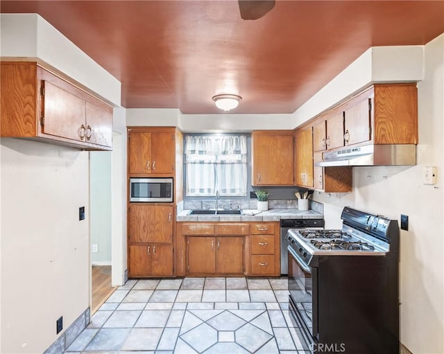 kitchen with light tile patterned flooring, sink, black gas range oven, and stainless steel microwave