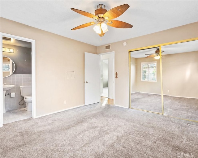 unfurnished bedroom with tile walls, carpet, ceiling fan, ensuite bath, and a closet