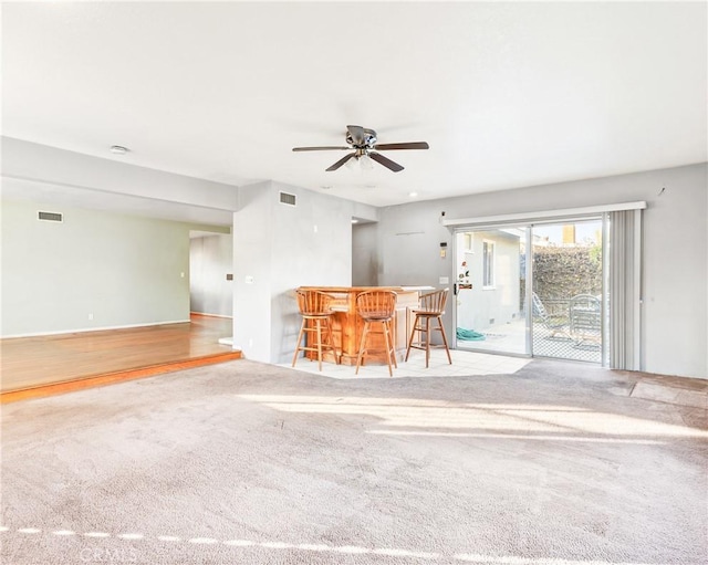 unfurnished living room featuring light colored carpet, ceiling fan, and bar area