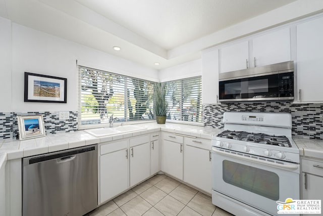 kitchen with sink, appliances with stainless steel finishes, tile counters, white cabinets, and backsplash