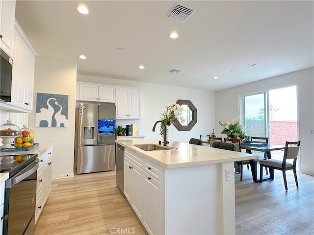 kitchen featuring sink, light hardwood / wood-style flooring, white cabinetry, stainless steel appliances, and an island with sink