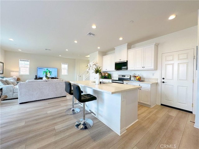 kitchen with white cabinets, a kitchen breakfast bar, light hardwood / wood-style floors, stainless steel appliances, and a center island with sink