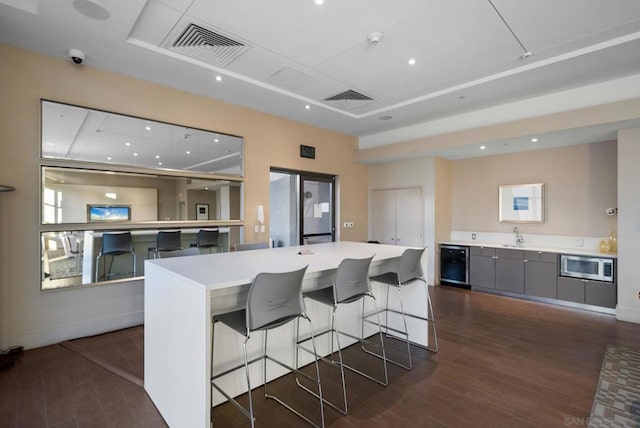 kitchen with stainless steel microwave, a kitchen breakfast bar, dark hardwood / wood-style flooring, and gray cabinetry