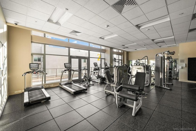 exercise room with a paneled ceiling, french doors, and a wall of windows