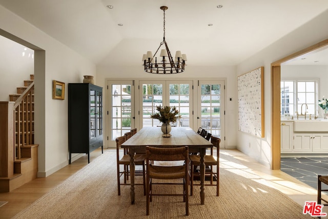 dining room featuring vaulted ceiling, a chandelier, sink, and light wood-type flooring