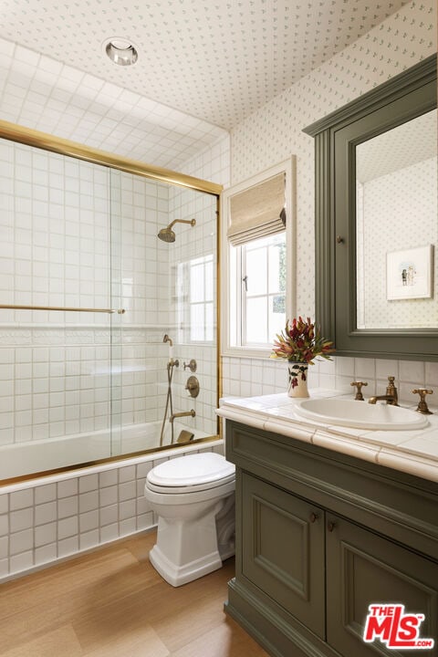 full bathroom featuring vanity, wood-type flooring, enclosed tub / shower combo, and toilet