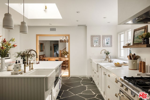 kitchen with sink, range, a skylight, hanging light fixtures, and white cabinets