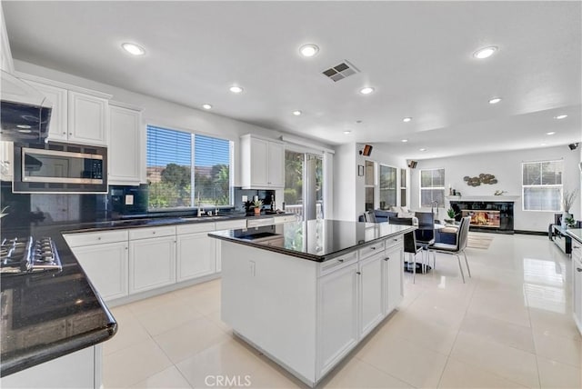 kitchen with white cabinetry, a multi sided fireplace, and appliances with stainless steel finishes