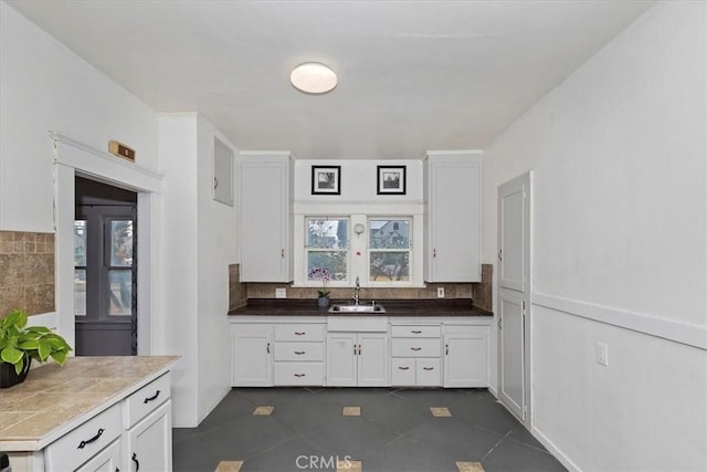 kitchen featuring plenty of natural light, dark tile patterned floors, sink, and white cabinets