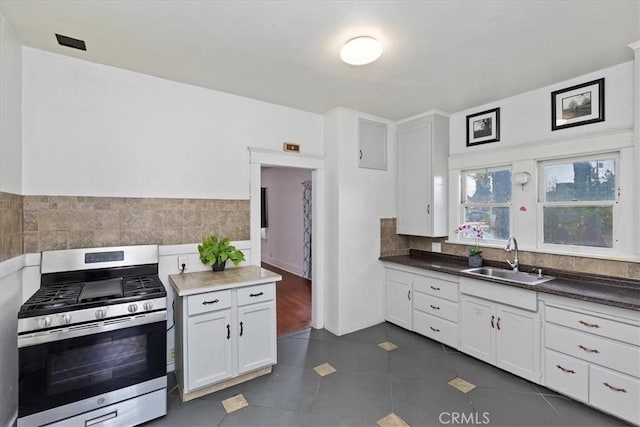 kitchen featuring sink, white cabinetry, tasteful backsplash, stainless steel gas range oven, and dark tile patterned flooring