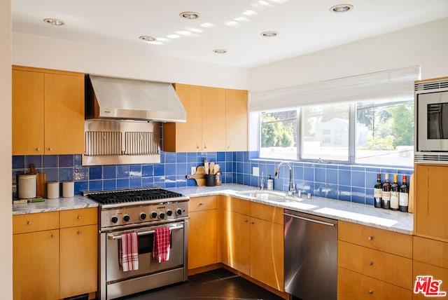 kitchen with tasteful backsplash, appliances with stainless steel finishes, sink, and wall chimney range hood