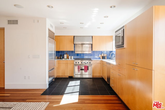 kitchen with tasteful backsplash, sink, built in appliances, light brown cabinets, and wall chimney exhaust hood