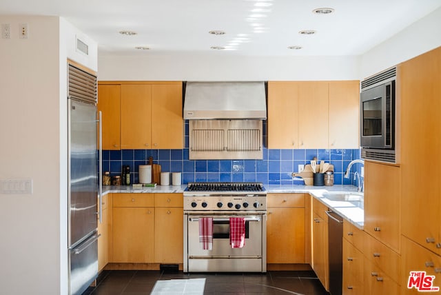 kitchen featuring wall chimney range hood, sink, dark tile patterned floors, backsplash, and built in appliances