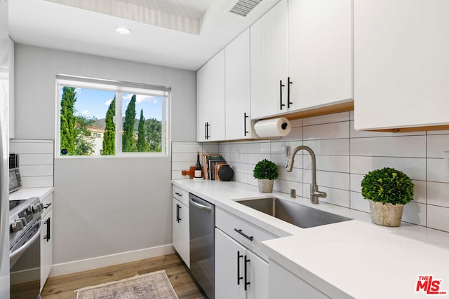 kitchen with tasteful backsplash, sink, white cabinets, stainless steel appliances, and light wood-type flooring