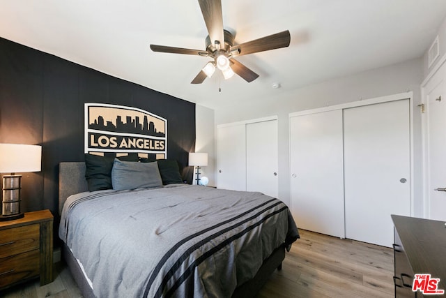 bedroom with ceiling fan, hardwood / wood-style flooring, and multiple closets