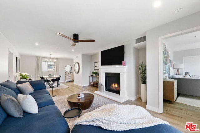 living room with ceiling fan with notable chandelier and light hardwood / wood-style flooring