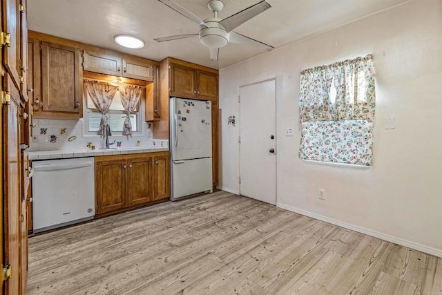 kitchen featuring white appliances, light wood-type flooring, tile counters, ceiling fan, and backsplash