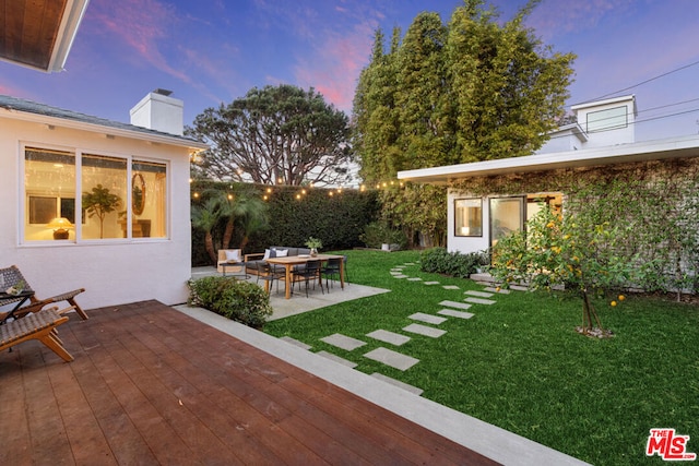 yard at dusk with a wooden deck, an outdoor hangout area, and a patio area