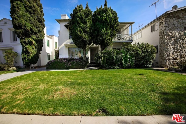 view of property hidden behind natural elements with a front lawn and a balcony