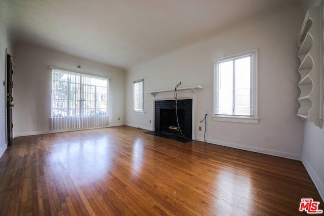 unfurnished living room featuring a tiled fireplace and dark hardwood / wood-style floors