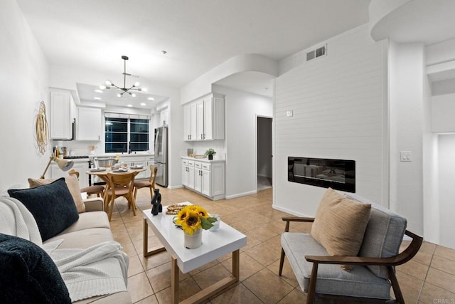 living room featuring a large fireplace, light tile patterned floors, and a notable chandelier