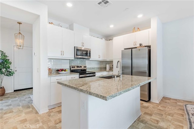 kitchen with appliances with stainless steel finishes, decorative light fixtures, sink, white cabinets, and a center island with sink