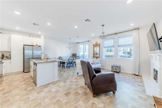 kitchen featuring appliances with stainless steel finishes, pendant lighting, white cabinets, a center island with sink, and an inviting chandelier