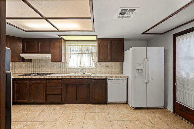 kitchen featuring light tile patterned flooring, sink, dark brown cabinets, white appliances, and decorative backsplash