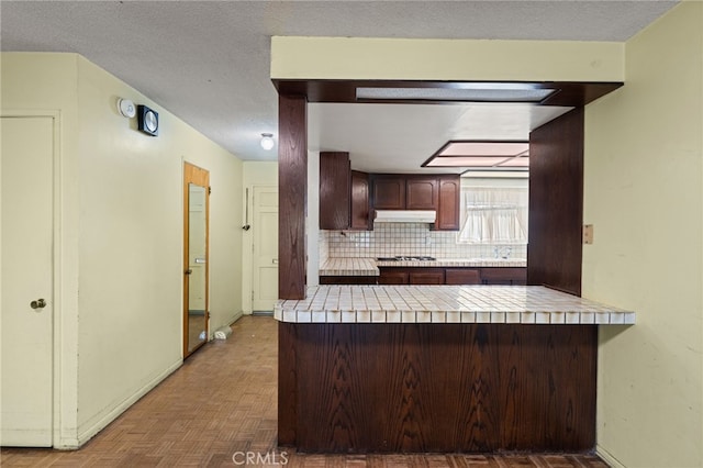 kitchen with tasteful backsplash, parquet flooring, dark brown cabinetry, and kitchen peninsula