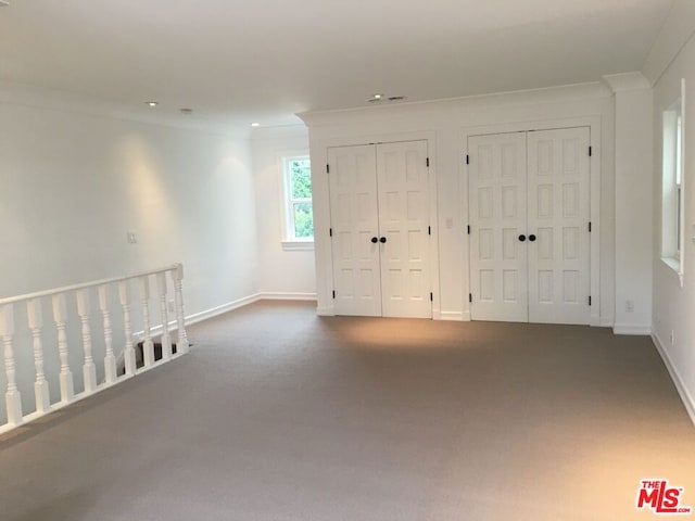 unfurnished bedroom with crown molding, carpet floors, and two closets