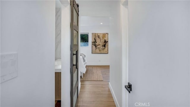 corridor featuring a barn door, wood finished floors, and baseboards