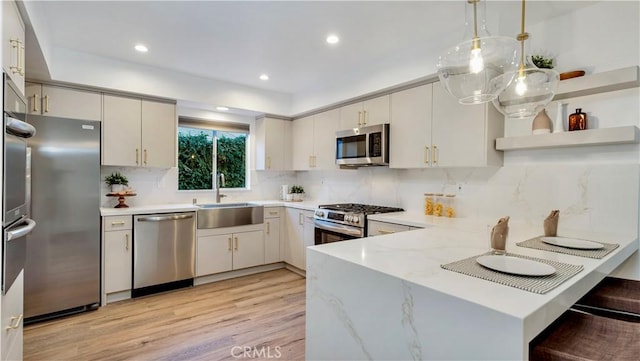 kitchen with pendant lighting, sink, stainless steel appliances, light stone counters, and kitchen peninsula