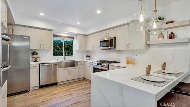 kitchen featuring light wood-style flooring, a sink, tasteful backsplash, stainless steel appliances, and a peninsula