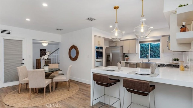 kitchen with pendant lighting, sink, light hardwood / wood-style flooring, a breakfast bar, and stainless steel appliances