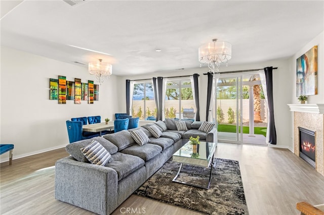 living room with an inviting chandelier, a tiled fireplace, plenty of natural light, and light wood-type flooring