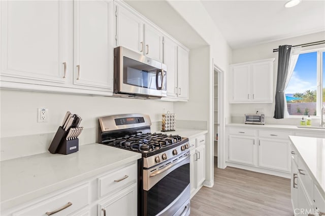 kitchen featuring appliances with stainless steel finishes, sink, light wood-type flooring, and white cabinets