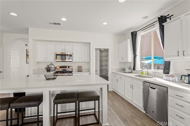 kitchen featuring sink, light hardwood / wood-style flooring, appliances with stainless steel finishes, white cabinets, and a kitchen bar