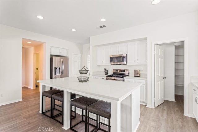 kitchen with white cabinetry, stainless steel appliances, a center island, and a kitchen bar