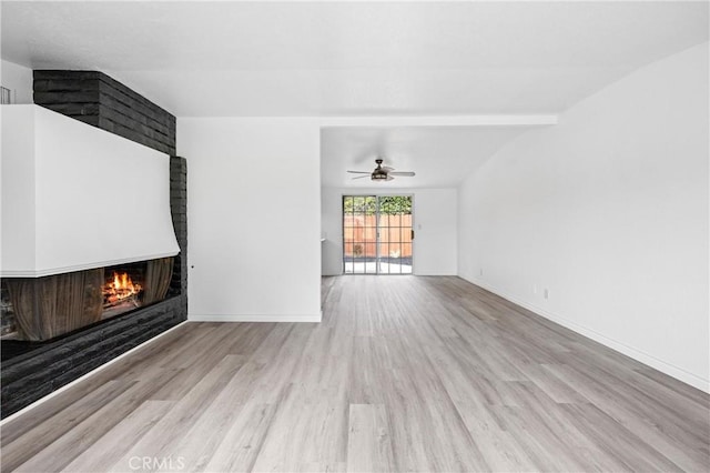 unfurnished living room featuring ceiling fan, a brick fireplace, and light wood-type flooring