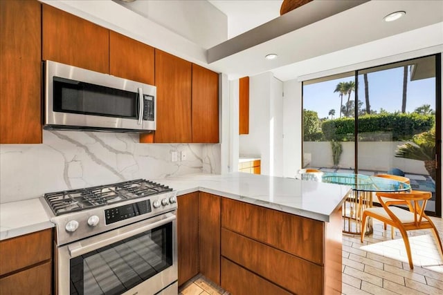 kitchen with appliances with stainless steel finishes, decorative backsplash, light stone counters, and kitchen peninsula