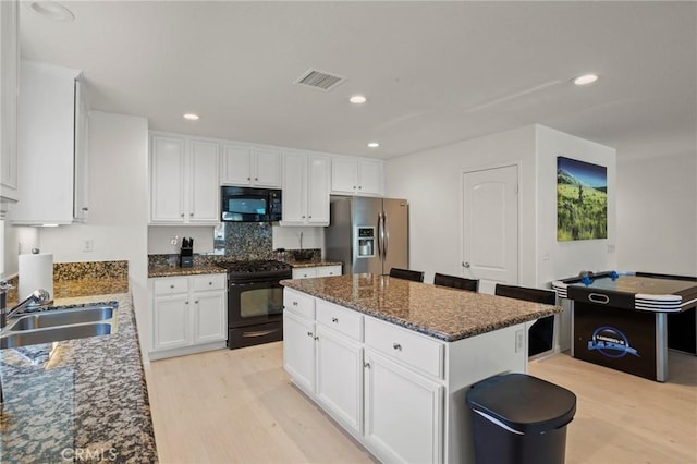 kitchen featuring sink, white cabinetry, dark stone countertops, black appliances, and a kitchen island