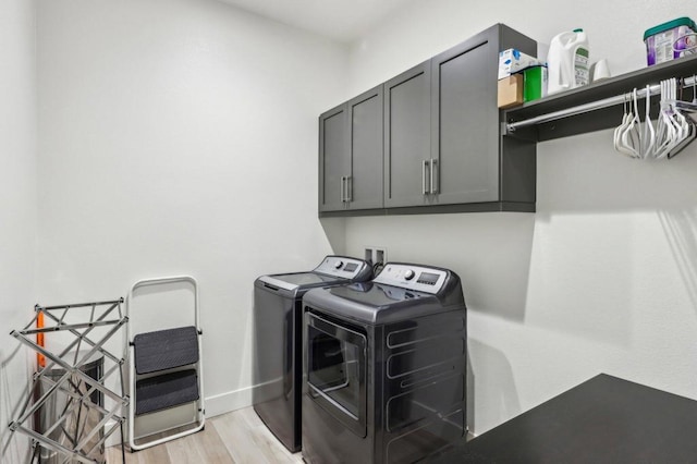 laundry room featuring cabinets, washing machine and clothes dryer, and light hardwood / wood-style flooring