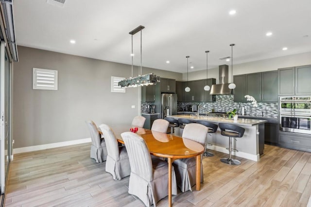 kitchen featuring wall chimney exhaust hood, a breakfast bar, hanging light fixtures, a center island with sink, and stainless steel appliances