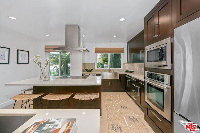 kitchen featuring sink, stainless steel appliances, a kitchen breakfast bar, tasteful backsplash, and island exhaust hood